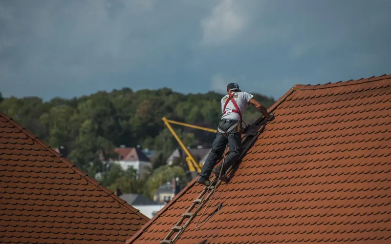 Roofer working on a sloped red-tiled roof, emphasizing the importance of quick estimates and lead management in the roofing industry during high-demand seasons.